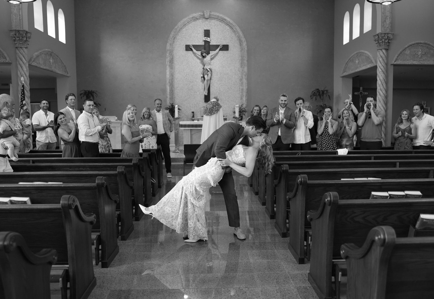 Black and white photo of a couple sharing a romantic dip kiss at the altar of a church during their wedding ceremony.