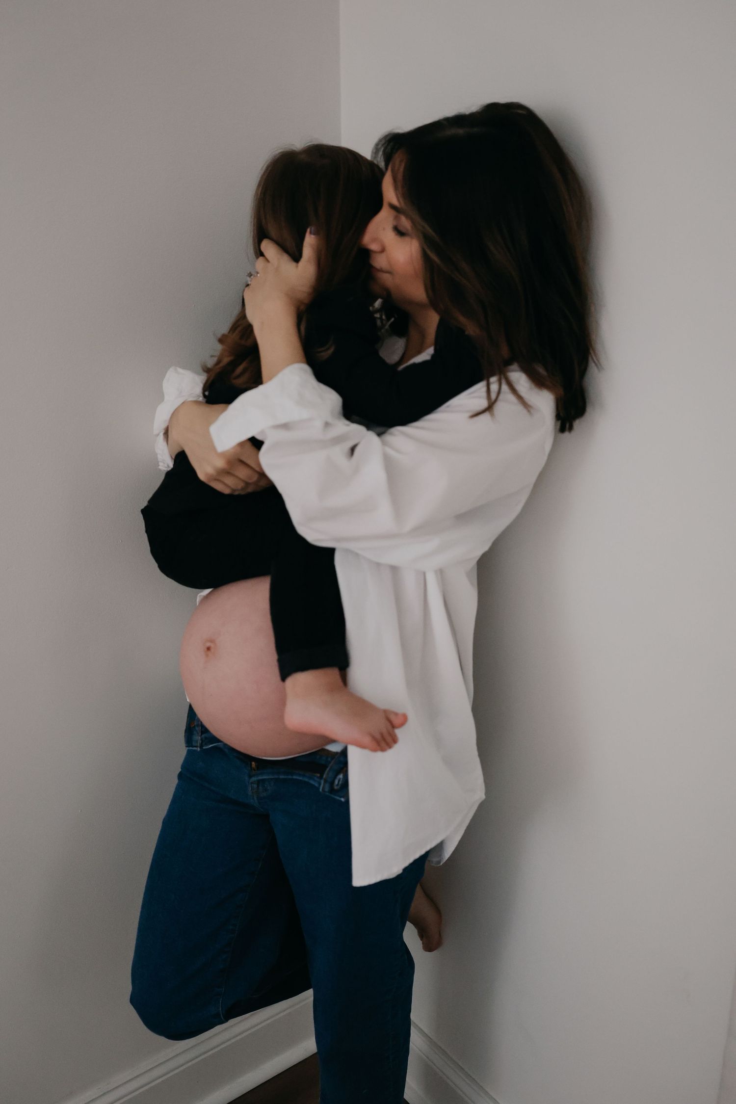 An intimate maternity photo showing a mother and child embracing against a gray wall.