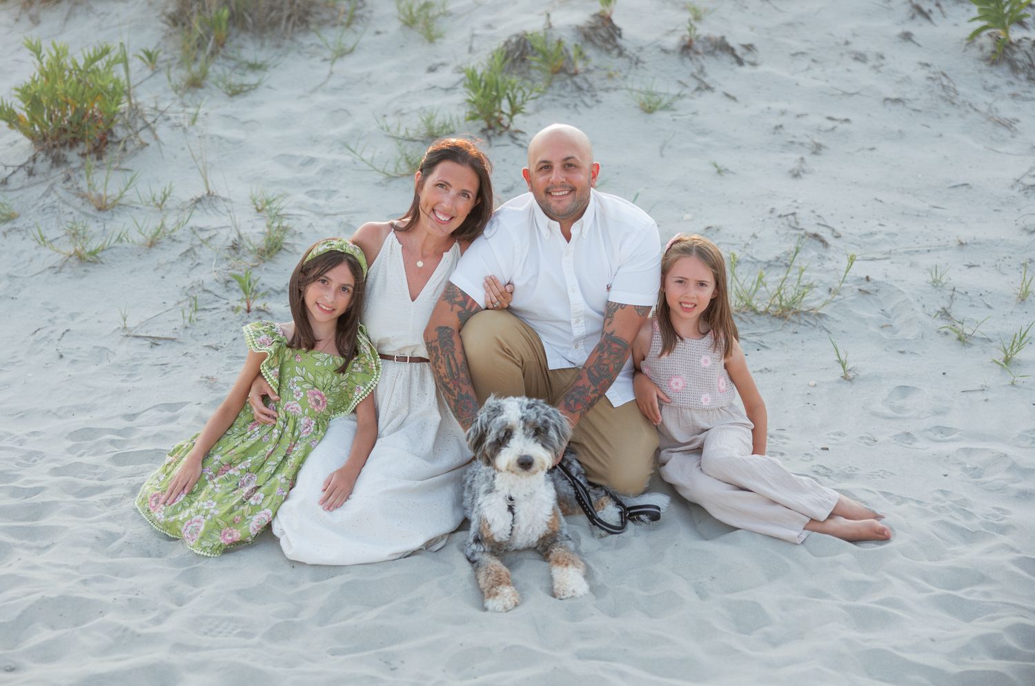 A couple with their dog relaxes on white sand beach during sunset for a maternity photography session.