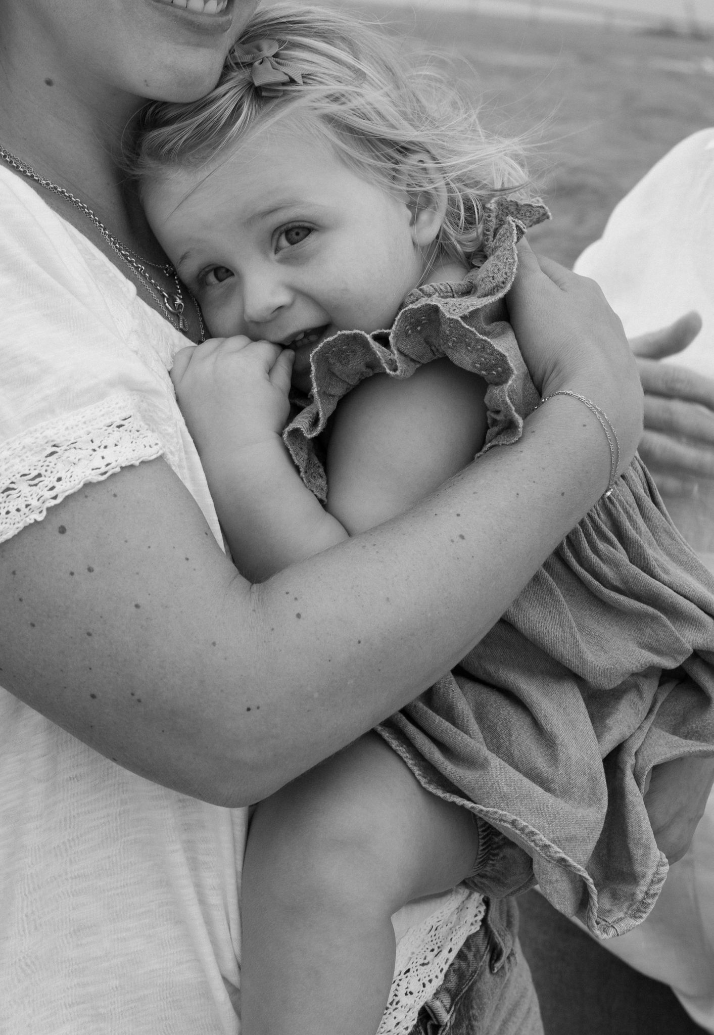 Black and white photo of a smiling toddler girl being held and cuddled by her mother in a tender embrace.