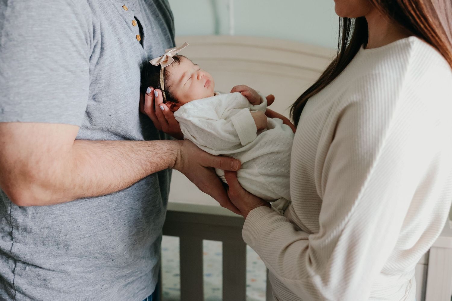Parents holding newborn baby together in nursery setting.