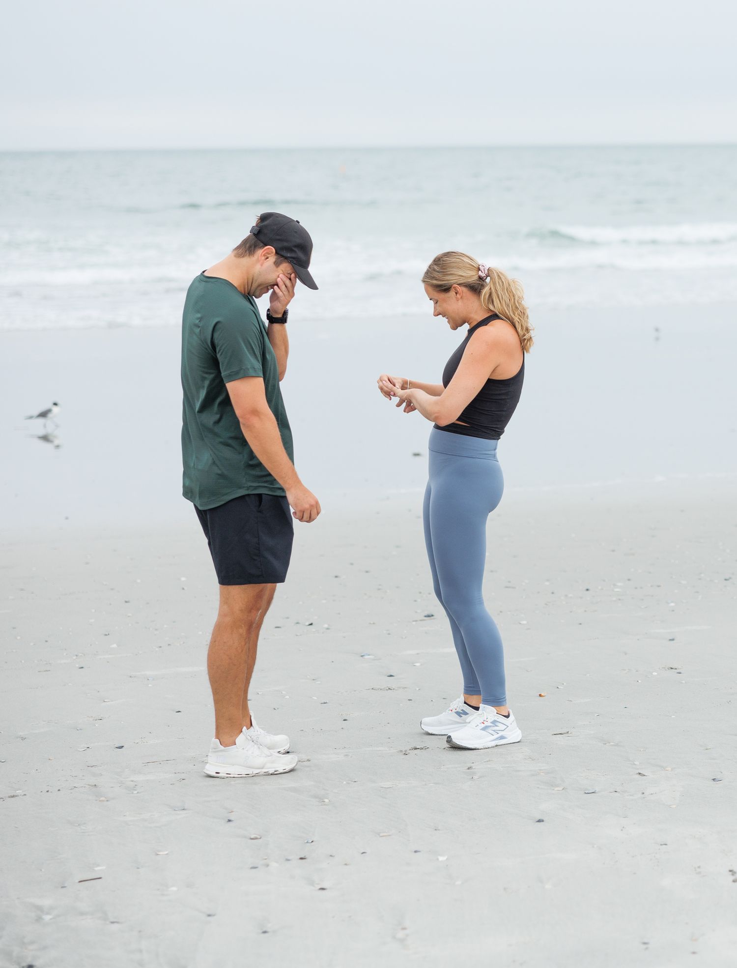 A proposal moment unfolds in sequence as a couple stands together on a sandy beach by the ocean.