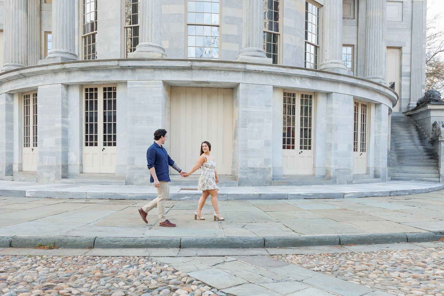 Couple dancing joyfully on a cobblestone street in front of a classic stone building with arched windows.