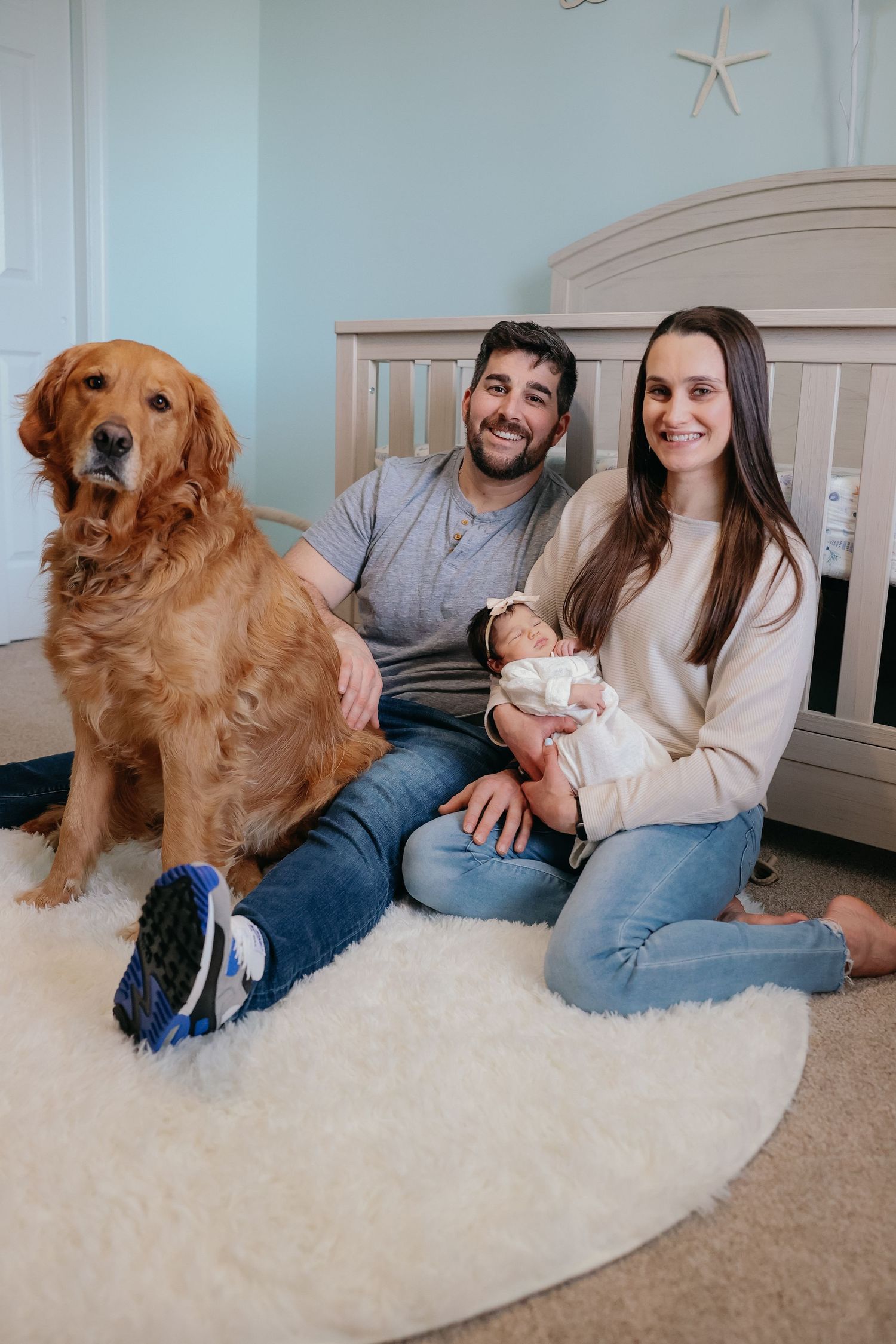 Family sitting on nursery floor with golden retriever dog near crib.