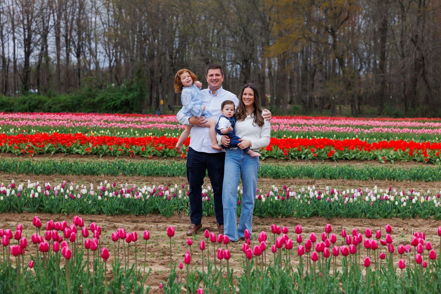 People pose amid colorful spring tulip fields as bright flowers bloom in neat rows across a vast garden landscape.