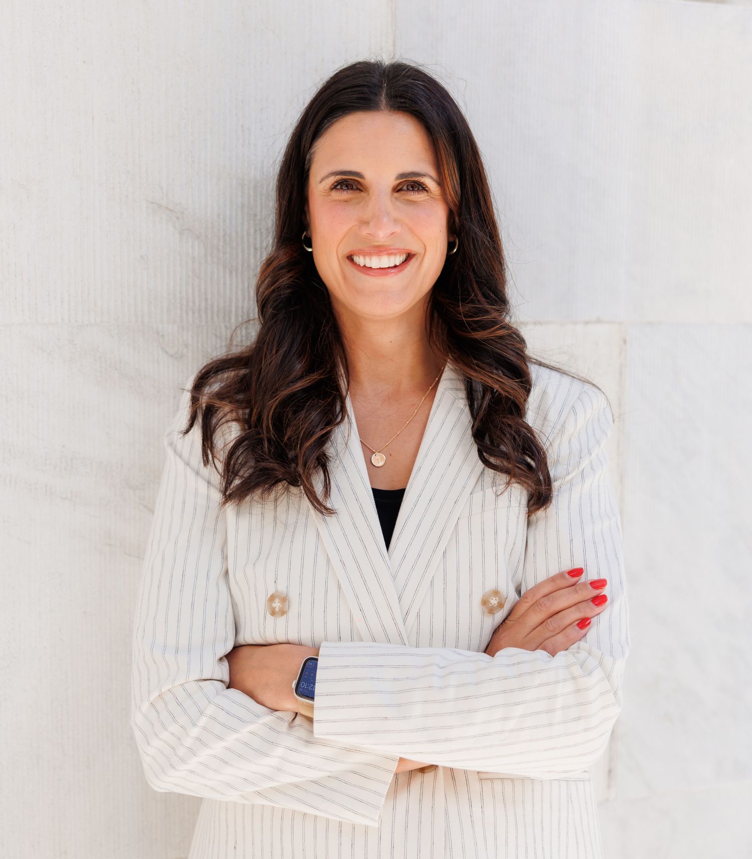 Professional woman in white striped blazer smiling with arms crossed against a marble wall.