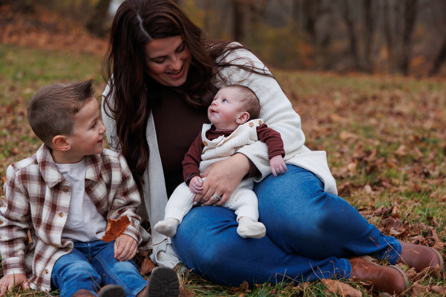 A series of outdoor autumn family photos with a baby wearing a blue sweater on fallen leaves.