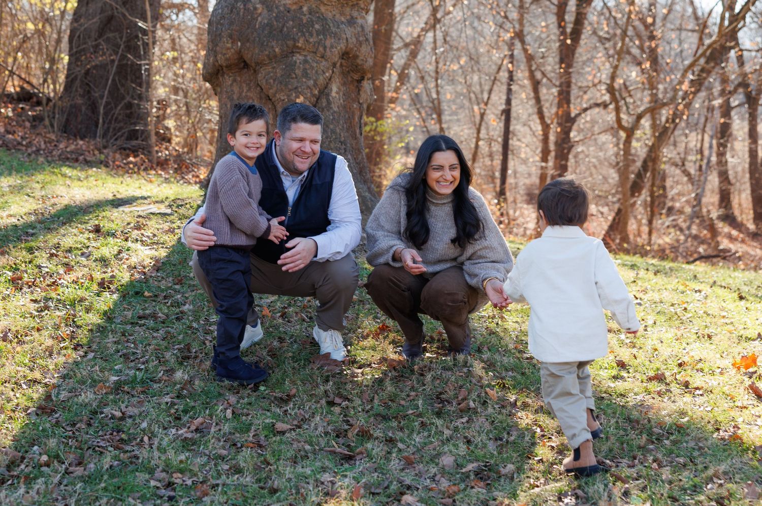 A family sits together outdoors on a sunny autumn day with fallen leaves scattered on the ground.