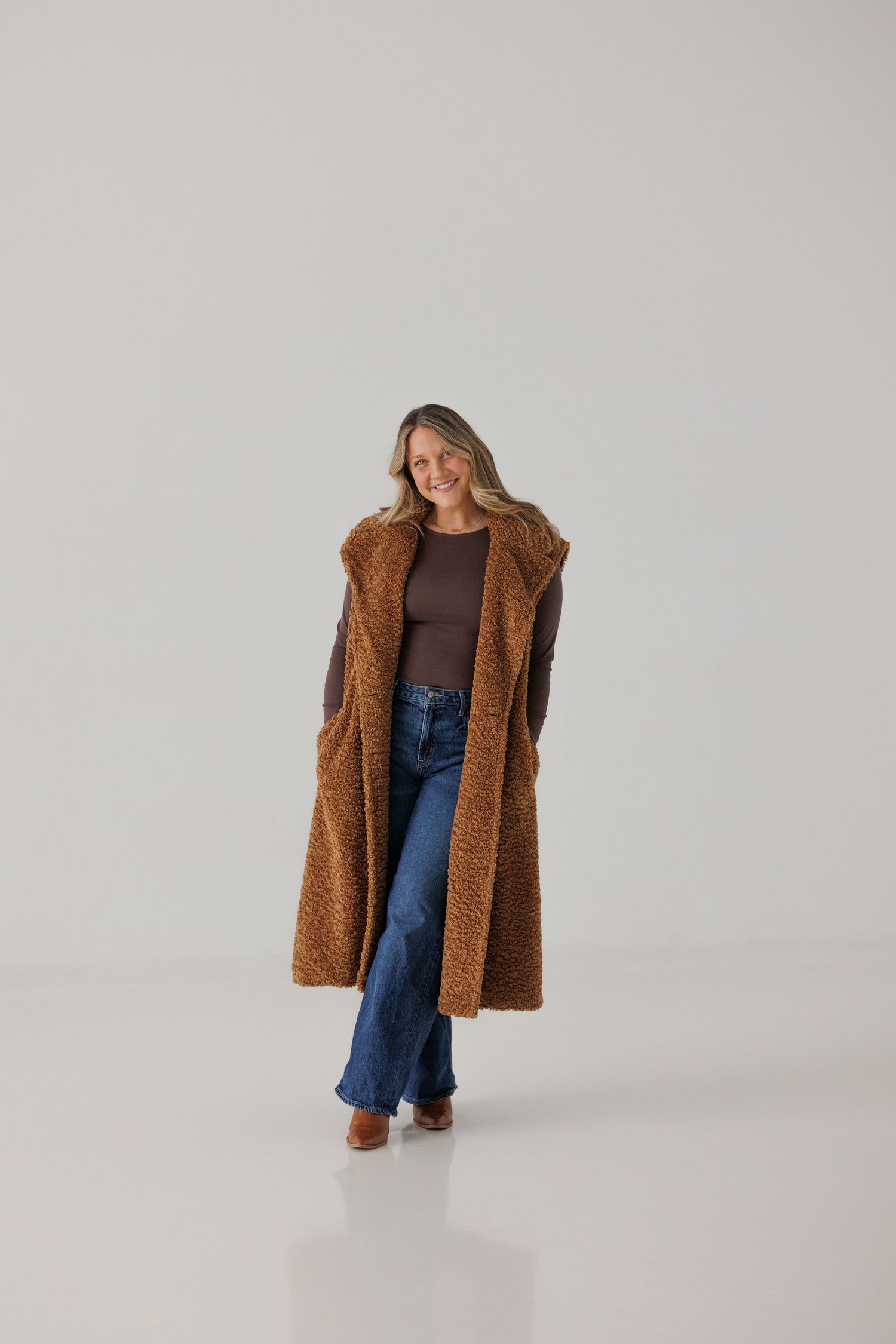 A fashionable brown teddy coat paired with jeans and a brown top in a minimalist studio setting.