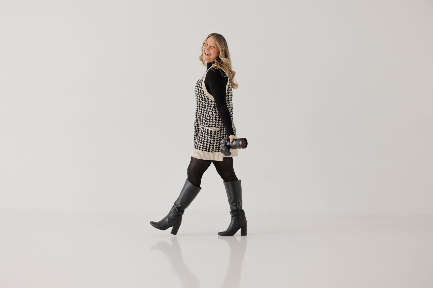 A stylish winter outfit featuring a houndstooth vest and knee-high boots against a white background.