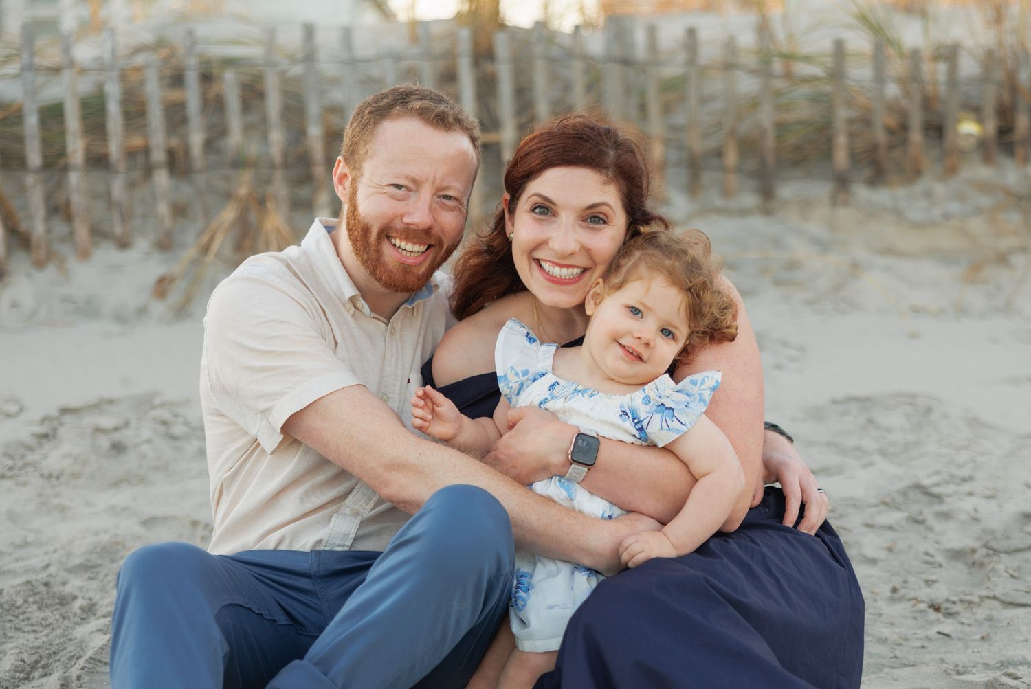 A family shares joyful moments together while sitting on a sandy beach at sunset.