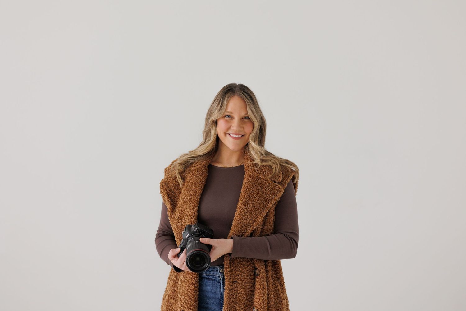 A brown teddy coat layered over a dark top and jeans in a minimalist studio setting.