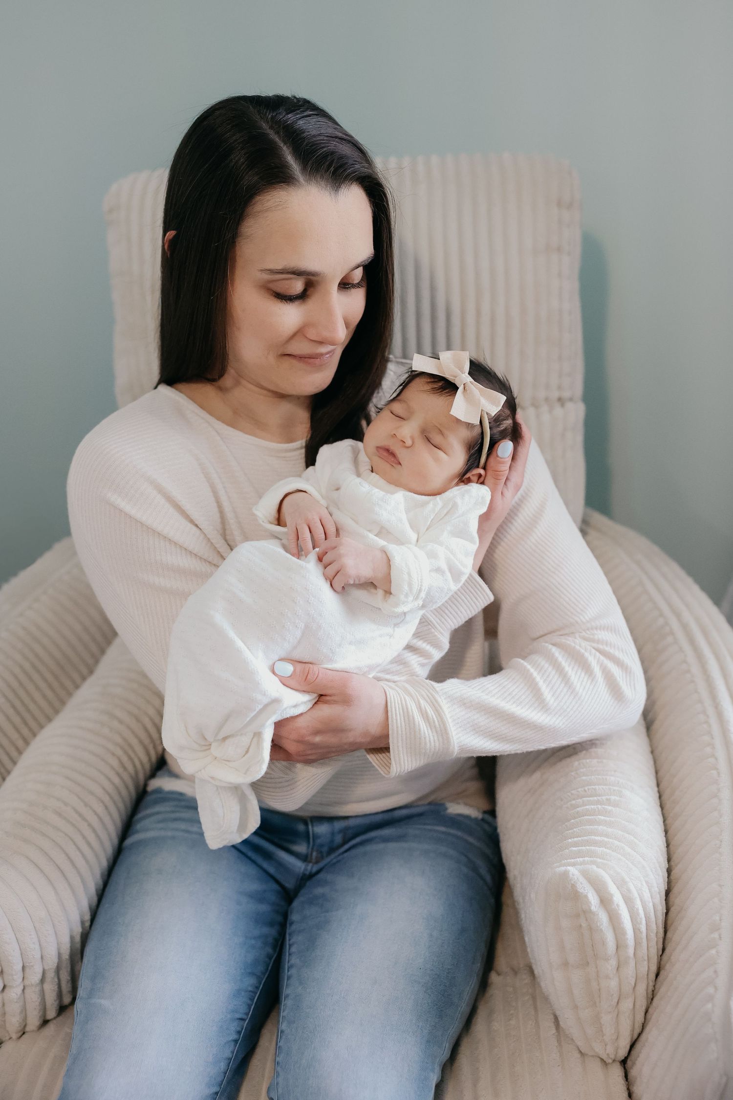 Tender moment between mother and sleeping infant in cozy armchair.