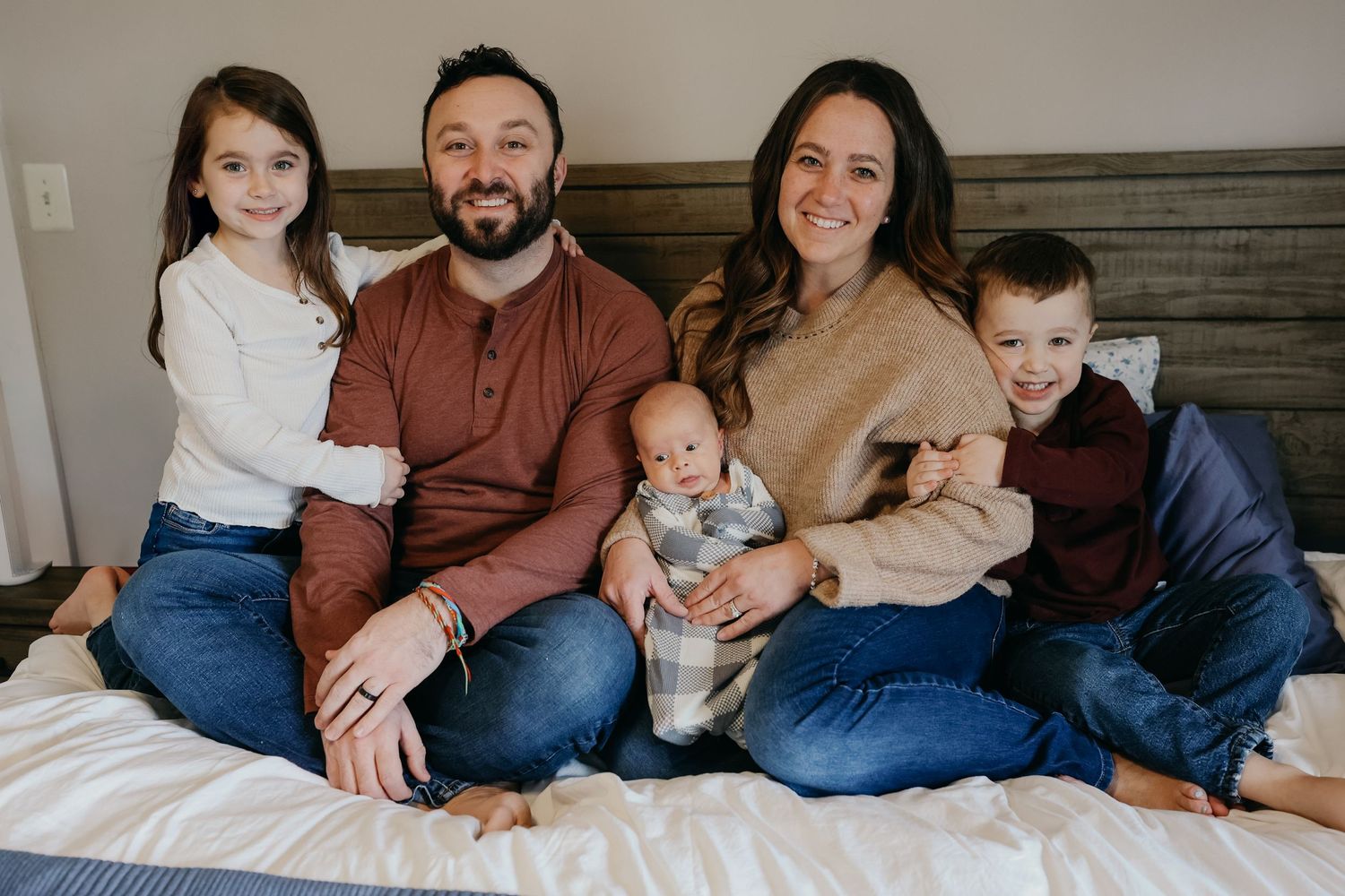 Family portrait on bed with three children and parents in casual clothing.