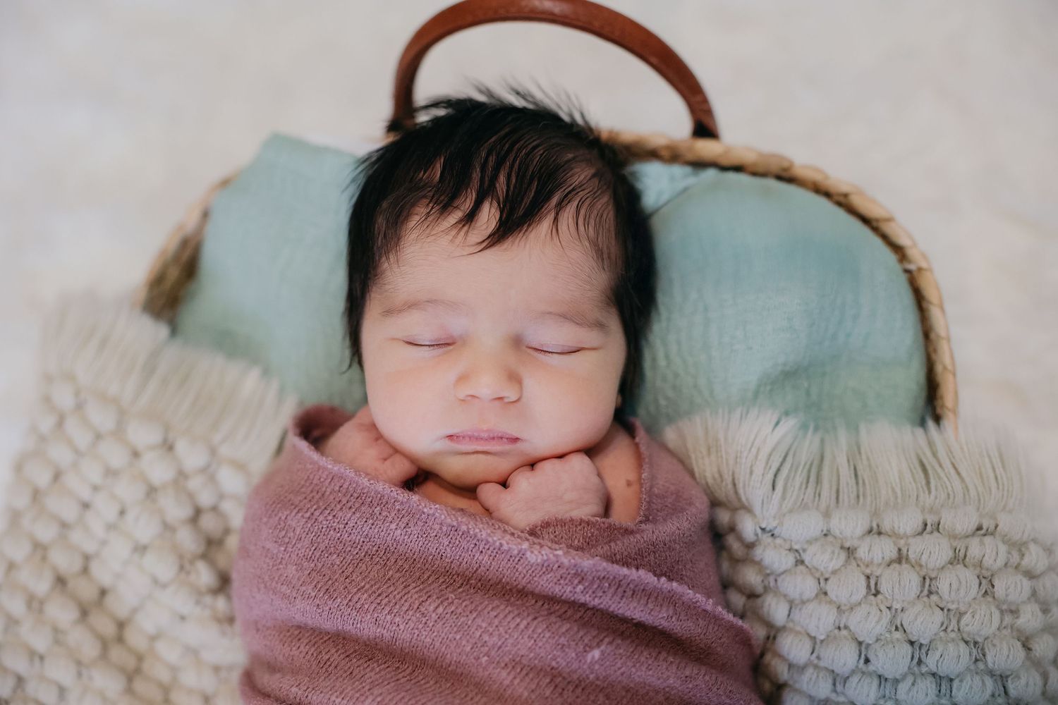 Sleeping baby wrapped in pink swaddle on textured white blanket.