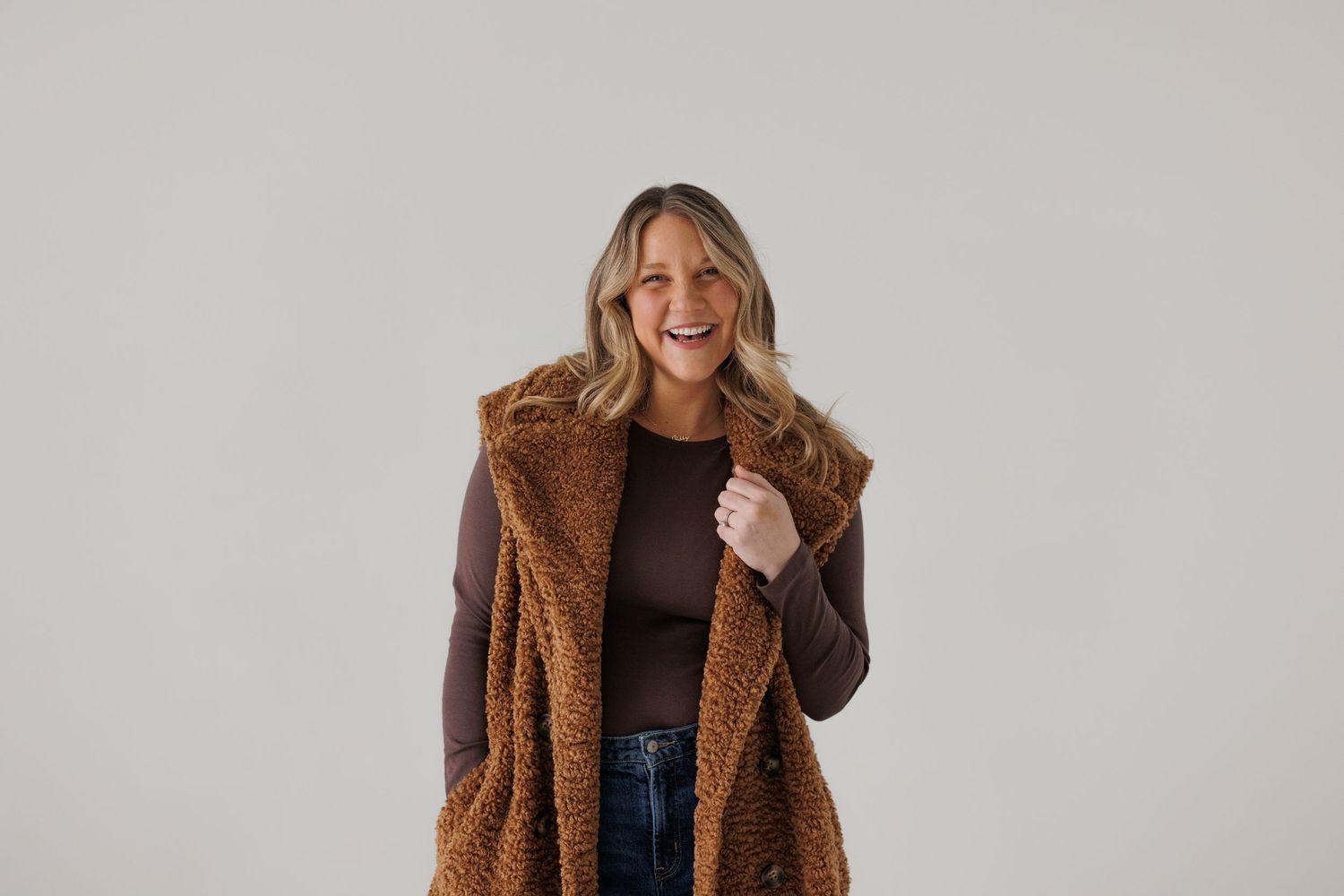 Woman in cozy brown teddy coat smiling against neutral studio background.
