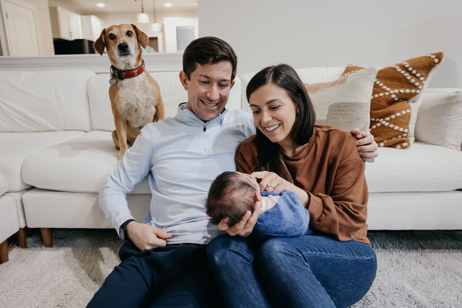 Family sitting on couch with dog sharing intimate moment in living room.