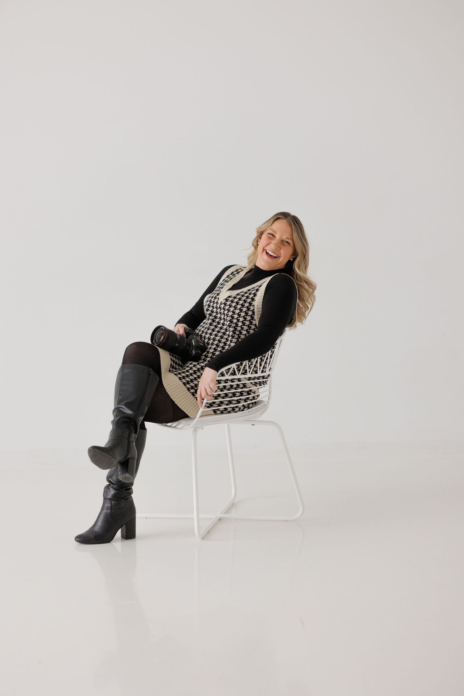 Professional fashion photo of someone posing in a black and white patterned sweater and boots on a white chair.