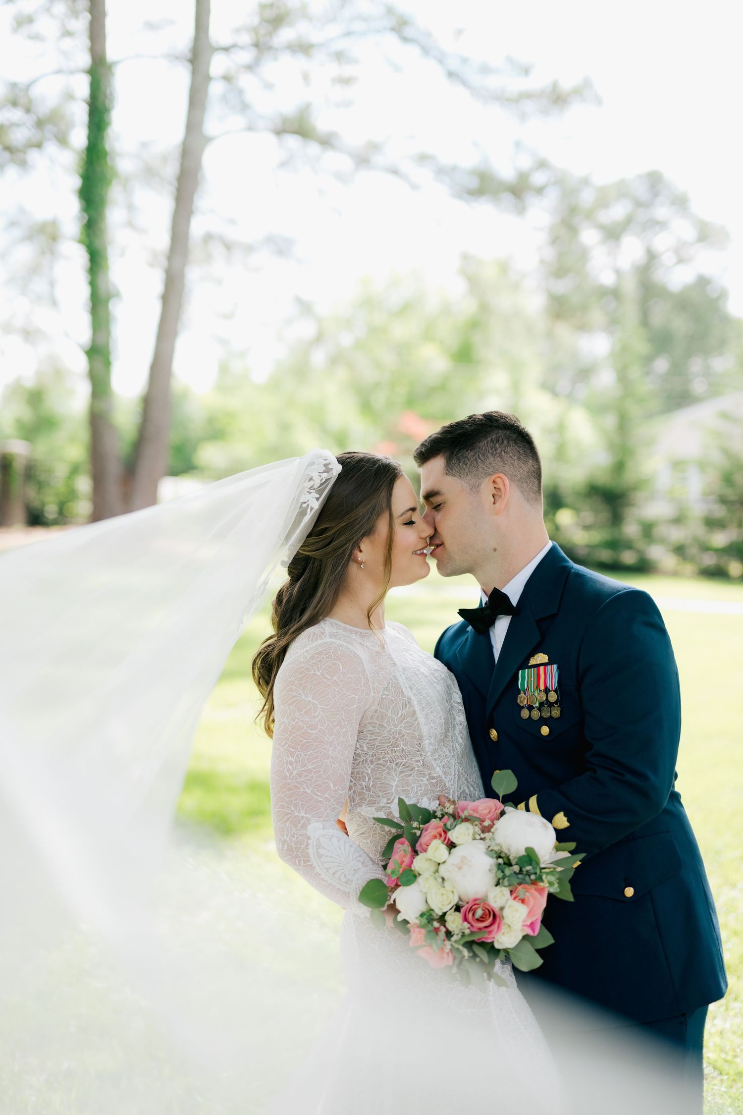 Military groom in dress uniform kisses bride as her veil blows in the breeze during a Virginia Beach wedding