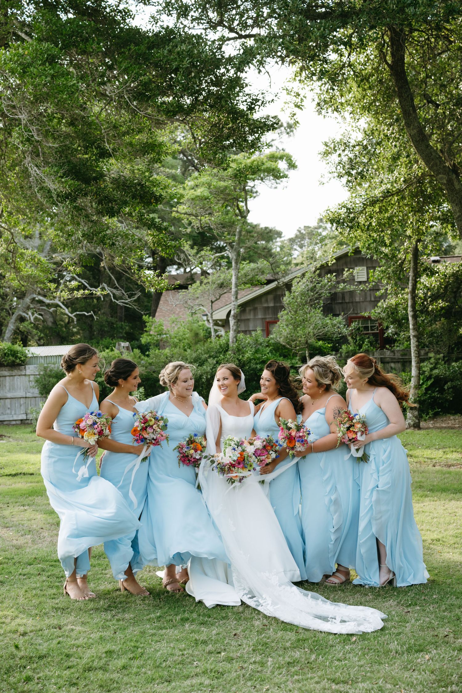 Bride in white gown surrounded by bridesmaids in light blue dresses  at The Westside Inn wedding in Manteo, NC.
