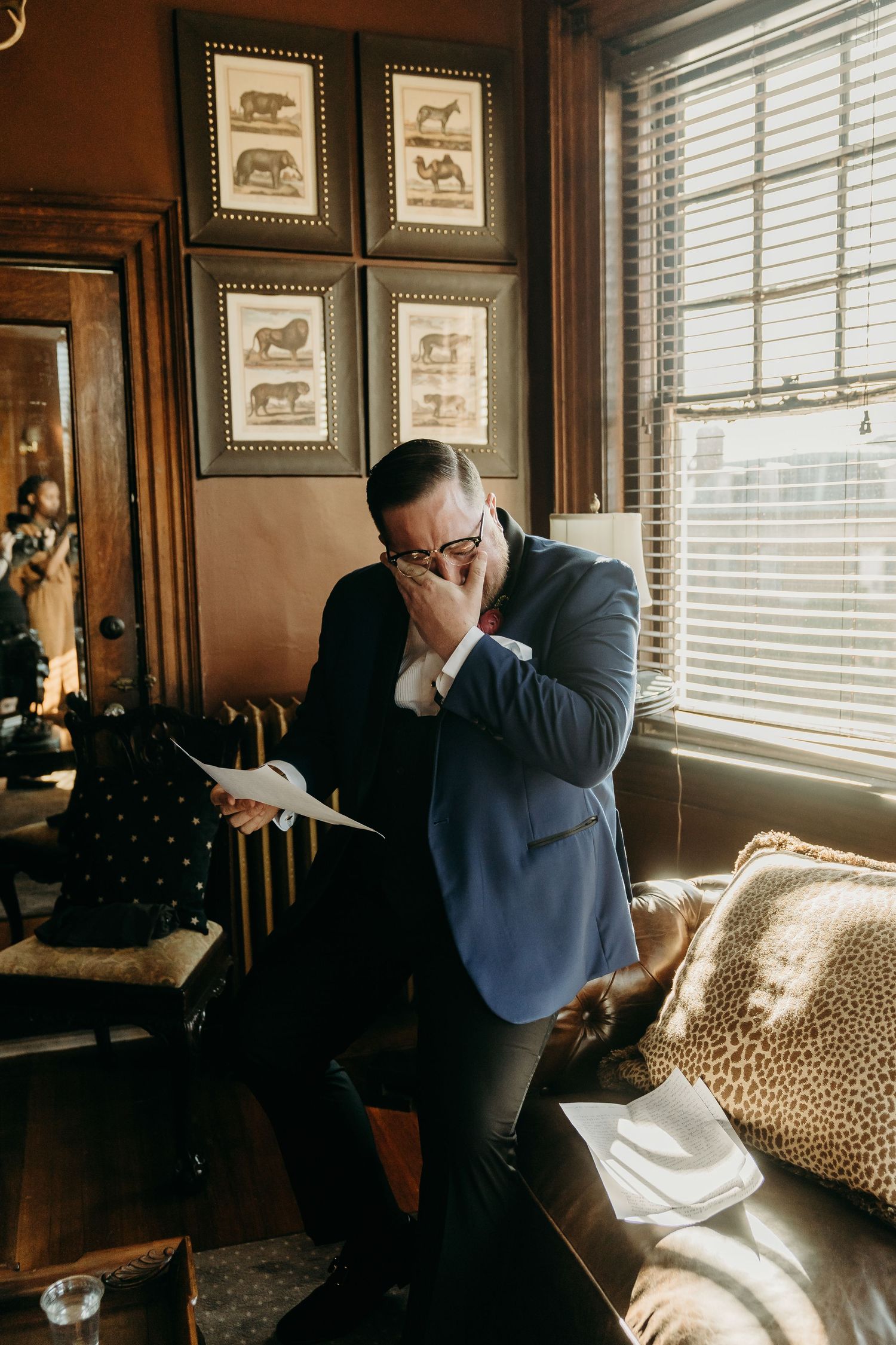 Groom in a blue blazer reads a heartfelt wedding letter from his wife by a window in a vintage room at Historic Martin Mansion in Virginia.