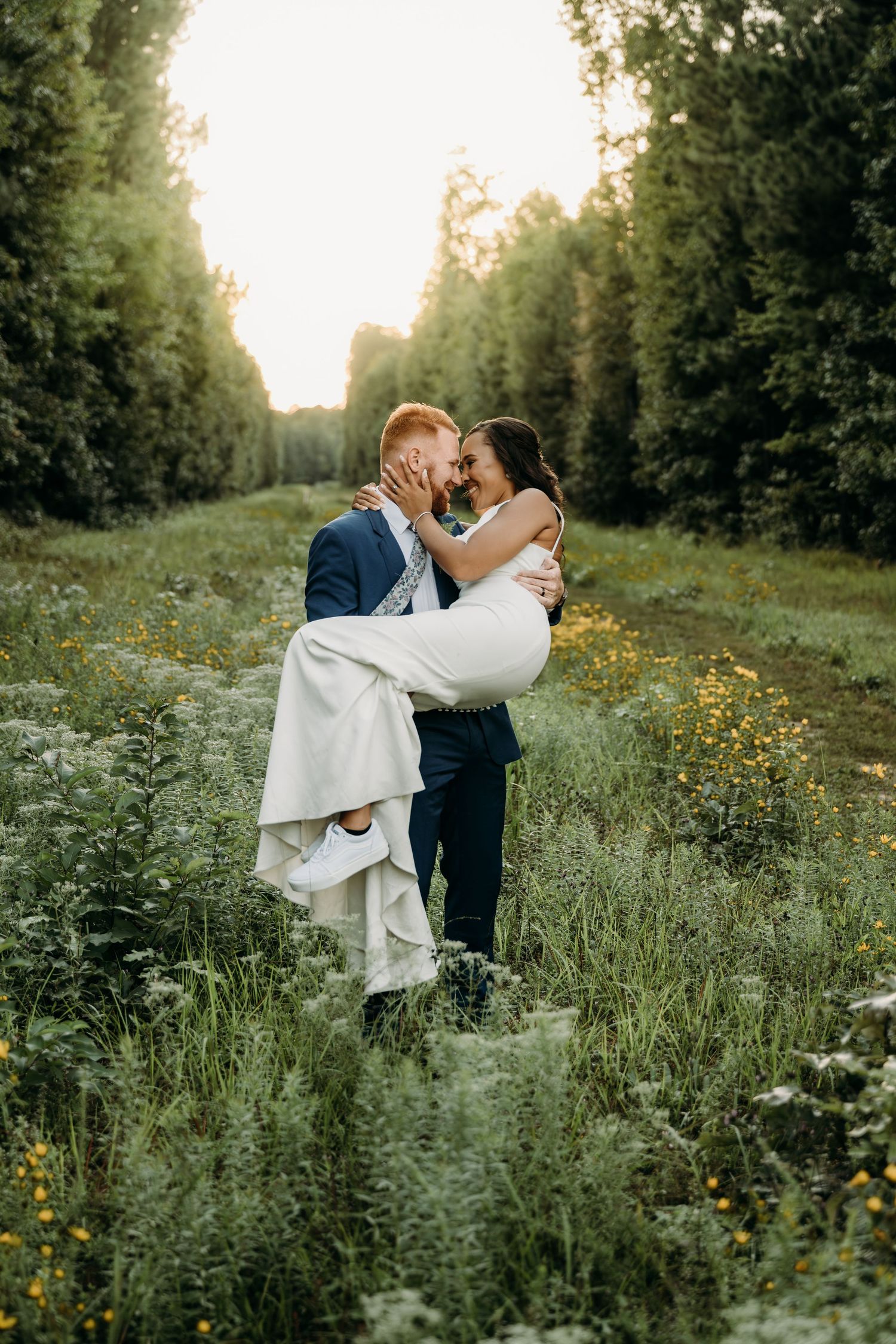 Bride and groom share a joyful kiss as he lifts her in a wildflower meadow at The Maine of Williamsburg wedding in Virginia.