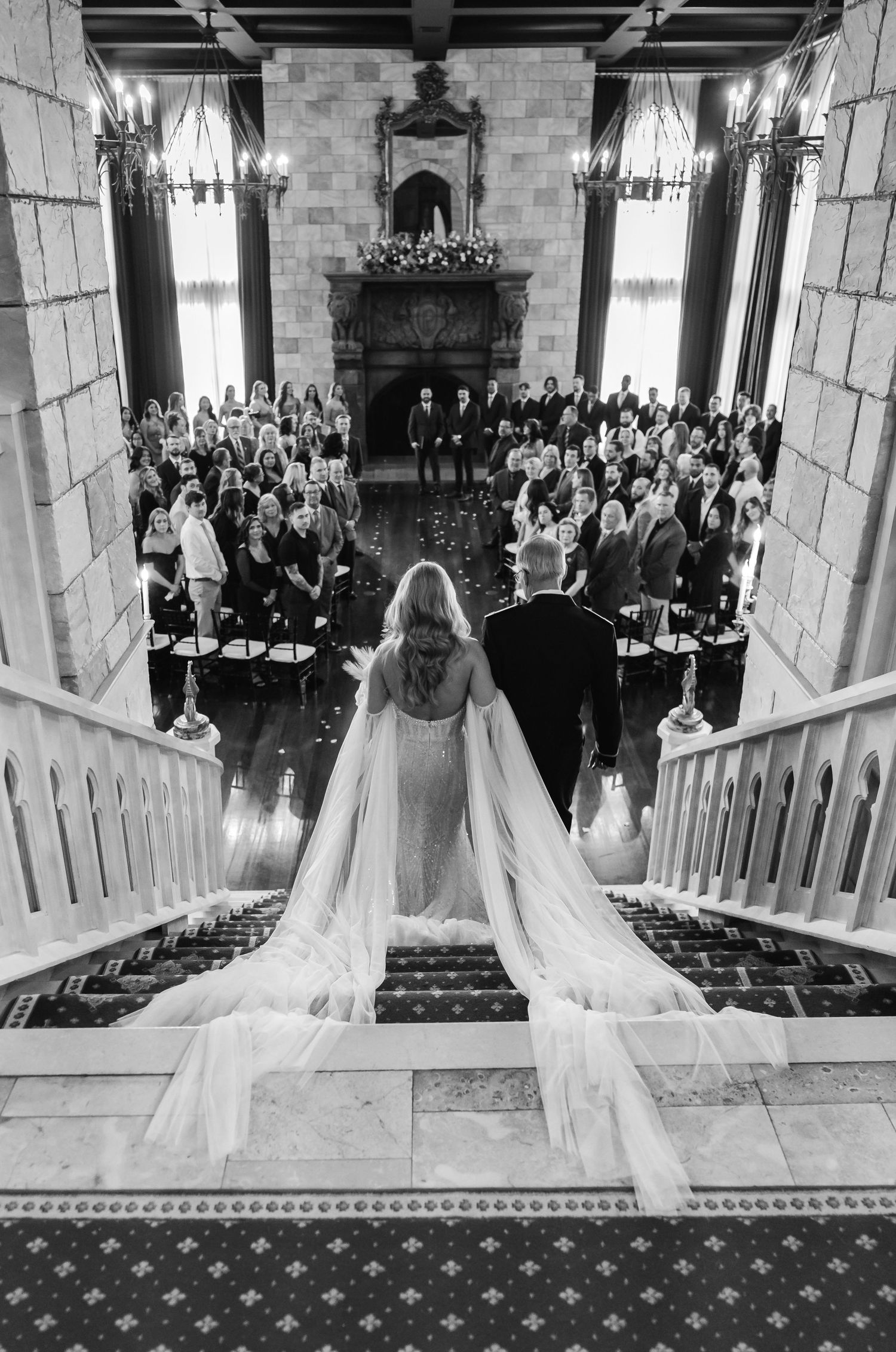 Black and white aerial photograph of bride descending a grand staircase toward wedding guests during her luxury wedding at Dover Hall in Vir
