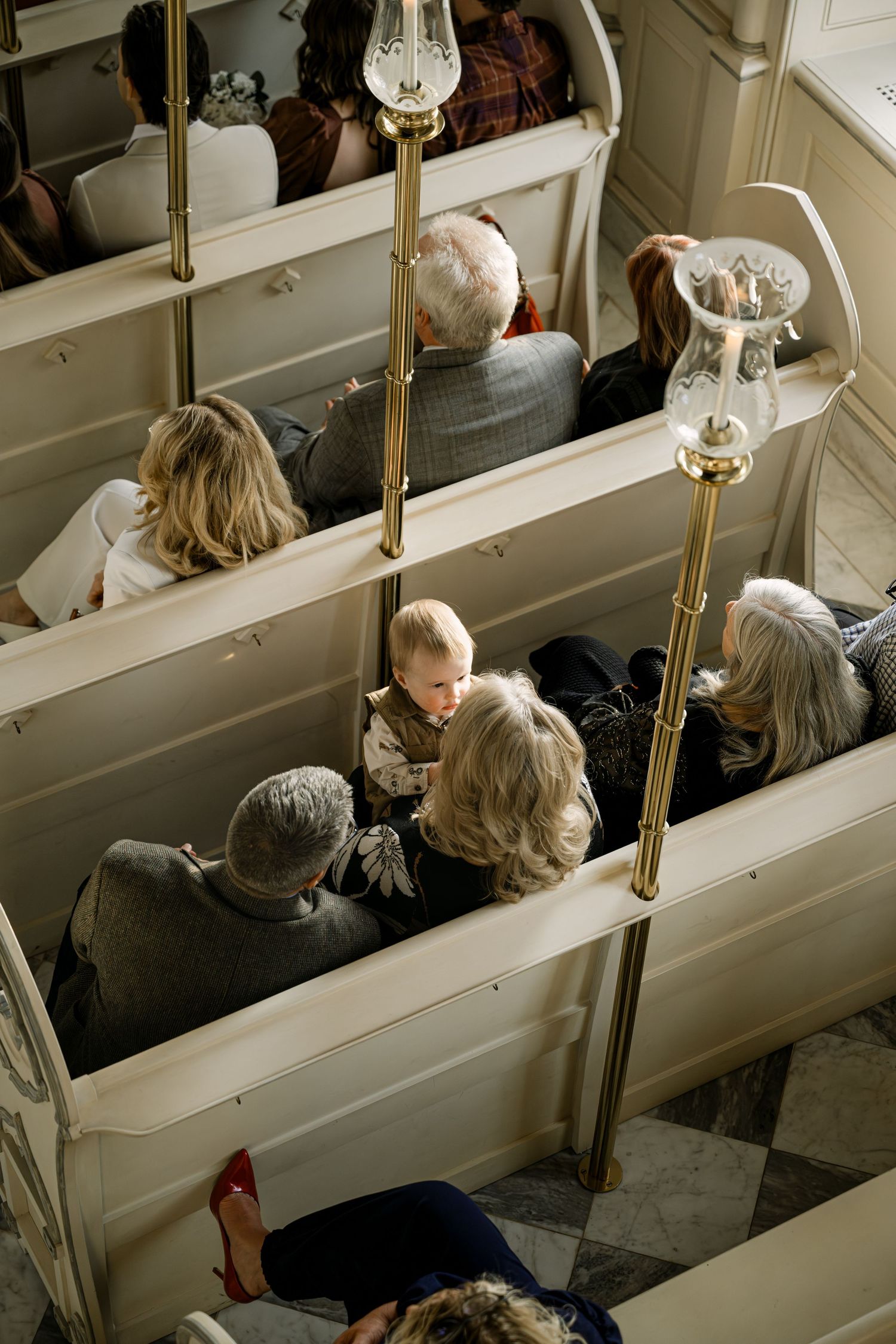 Aerial view of wedding guests seated in elegant white church pews with gold candle holders at Trump Winery Chapel.