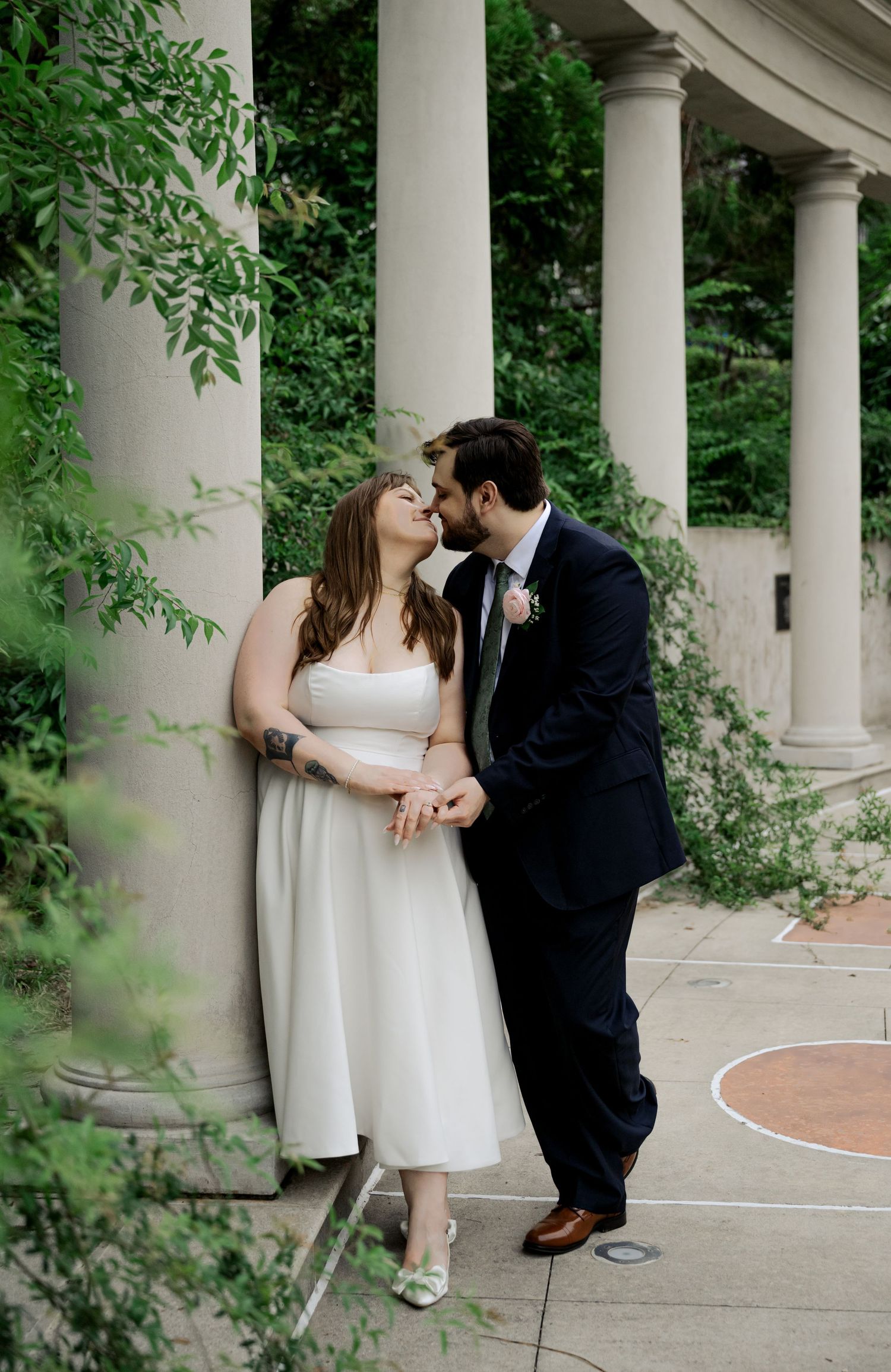 Bride and groom share a tender kiss beside elegant stone columns in a lush garden wedding setting in Atlanta Georgia