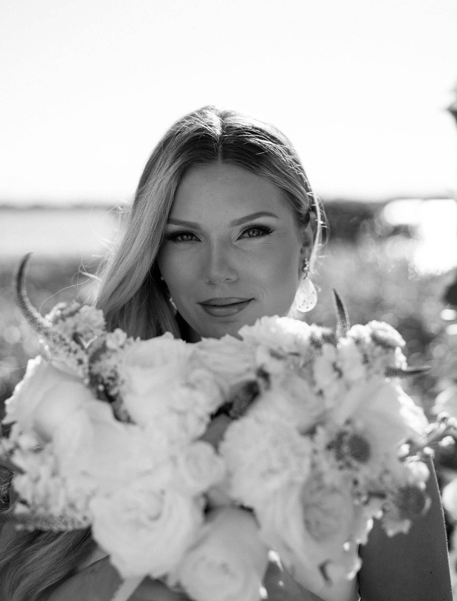 Black and white bridal portrait of a blonde woman holding a large bouquet of roses outdoors.