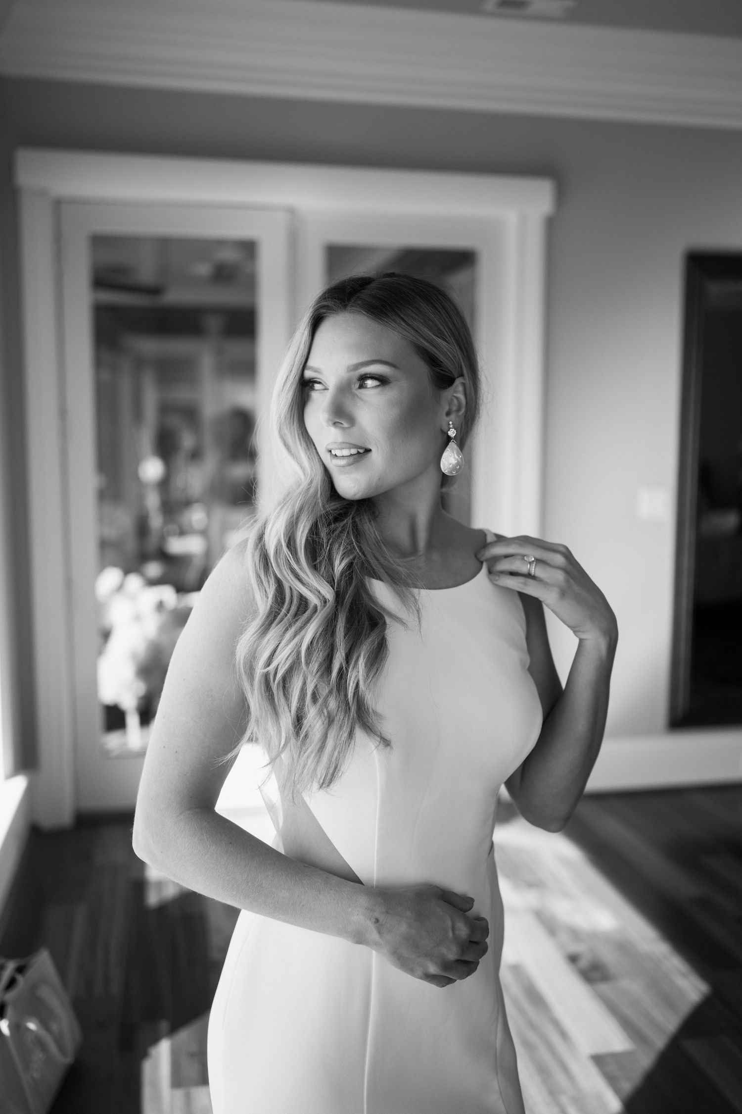 Bride in a sleek white gown and drop earrings smiles in a timeless black and white portrait at a Virginia family estate wedding.