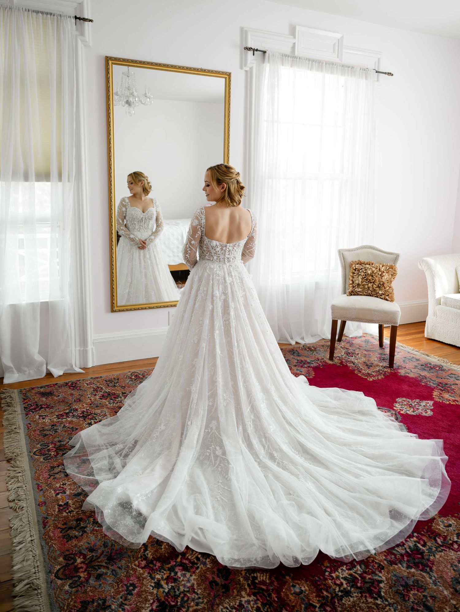 Bride in lace ball gown with long train views reflection in gold mirror.