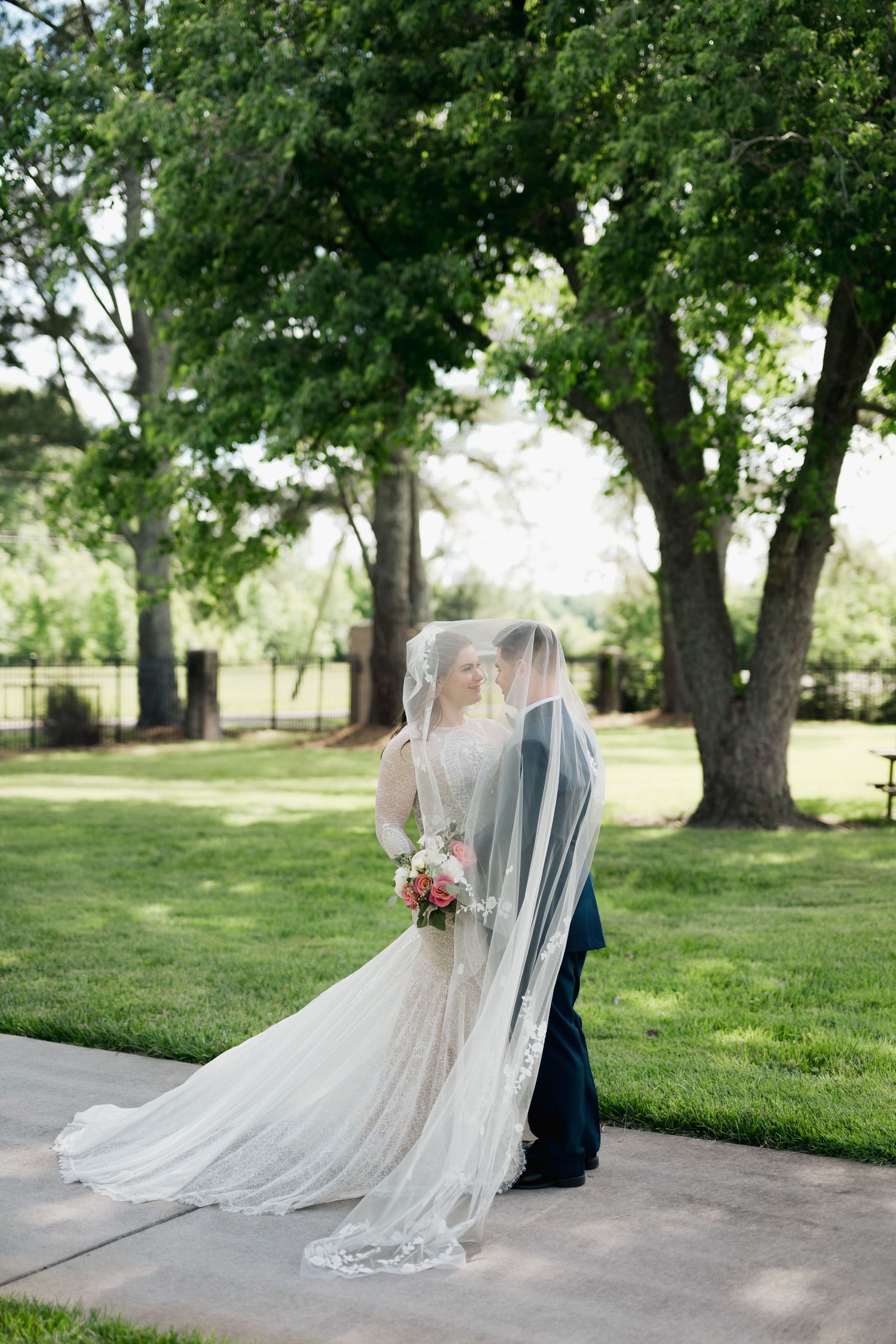 Bride and groom share romantic kiss under flowing lace veil in a serene green garden setting Virginia Beach wedding