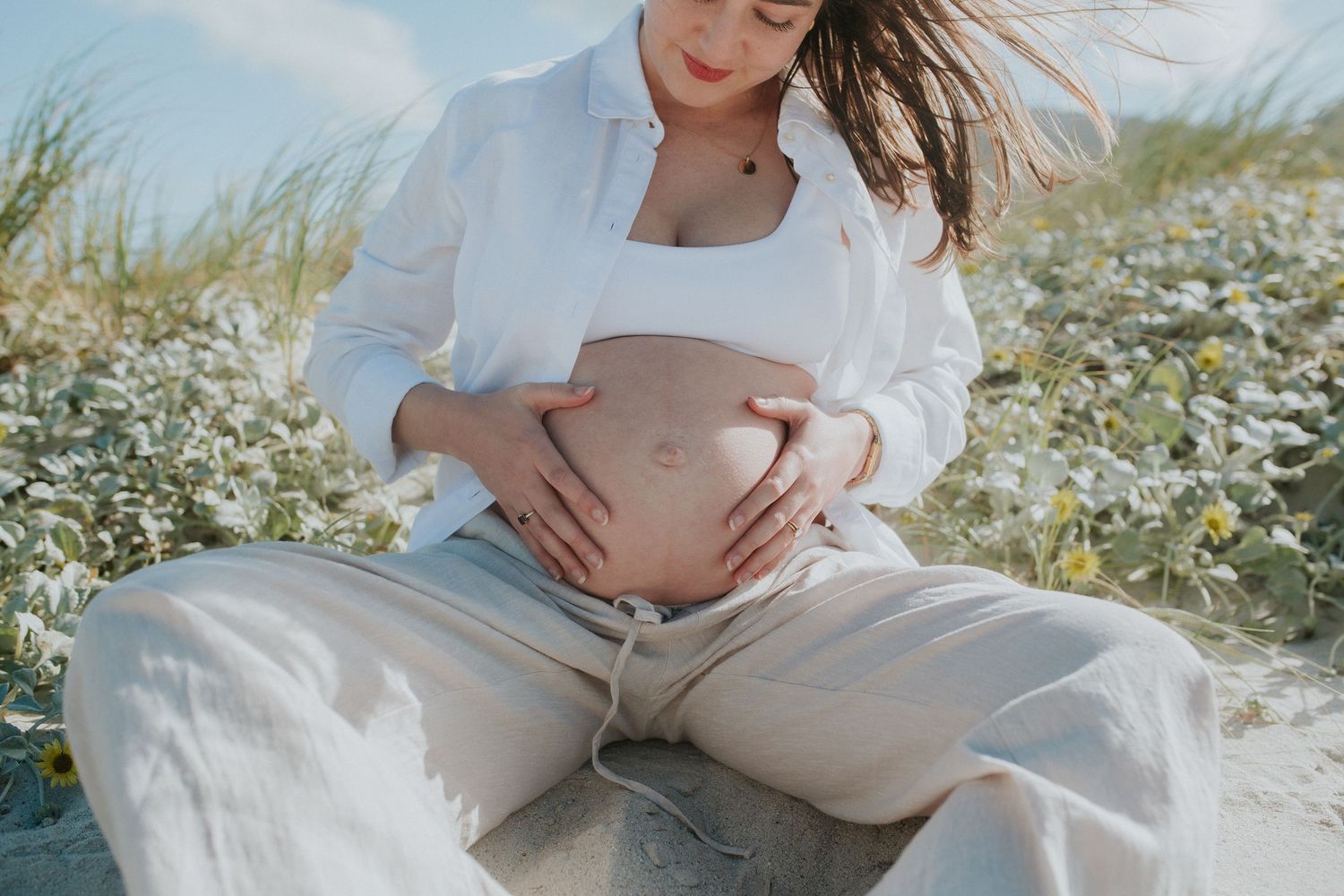 woman sitting on sand cradles bump in maternity shoot at muizenberg beach