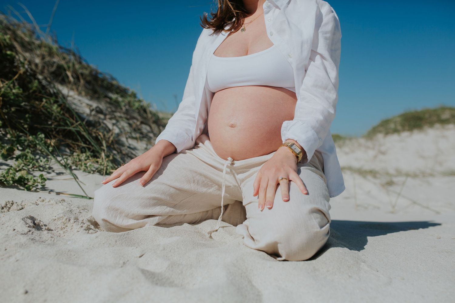 Woman kneels in the sand showing her baby bump