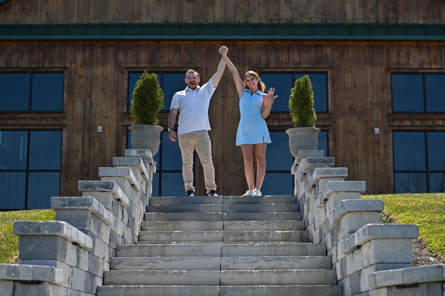 People walking down stone steps at an outdoor venue with white stone railings and a rustic wooden backdrop.