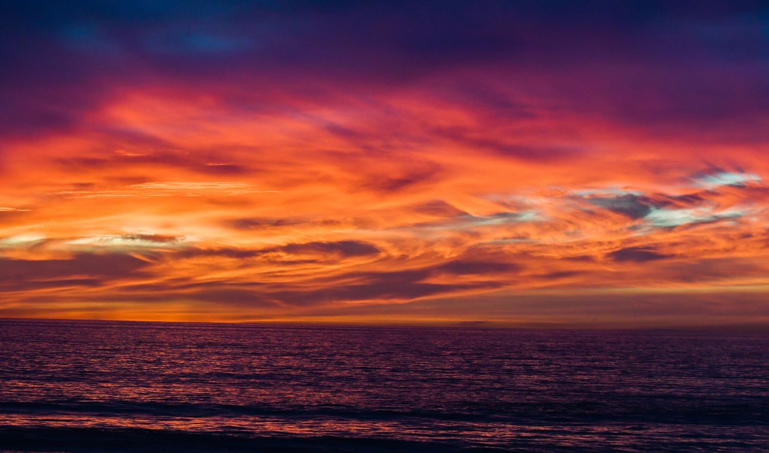 Vivid orange and red sunset over calm ocean waters with dramatic clouds illuminating the sky.