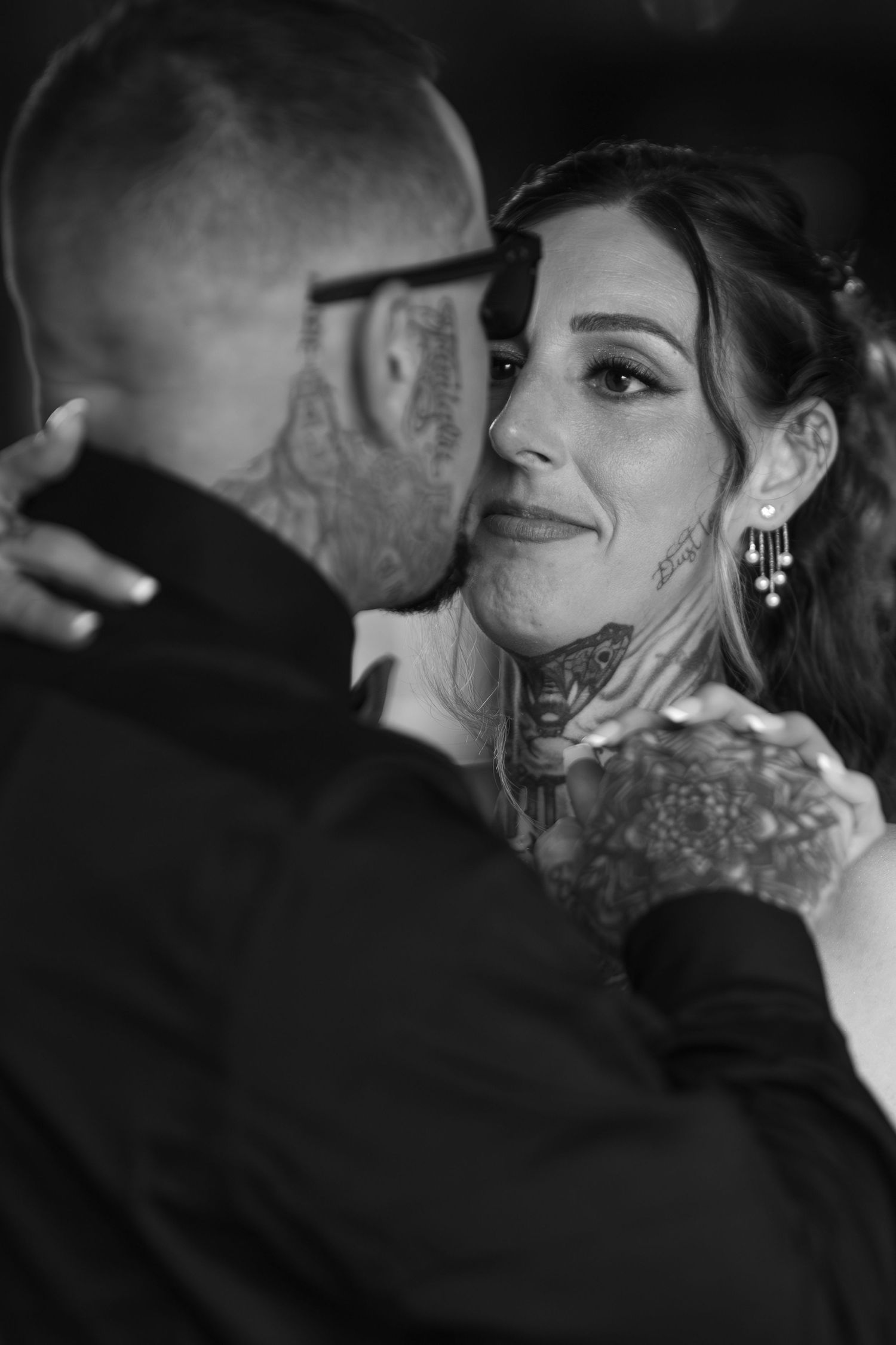 Black and white photo of a tattooed couple sharing an intimate moment, the bride smiling warmly during their wedding dance.