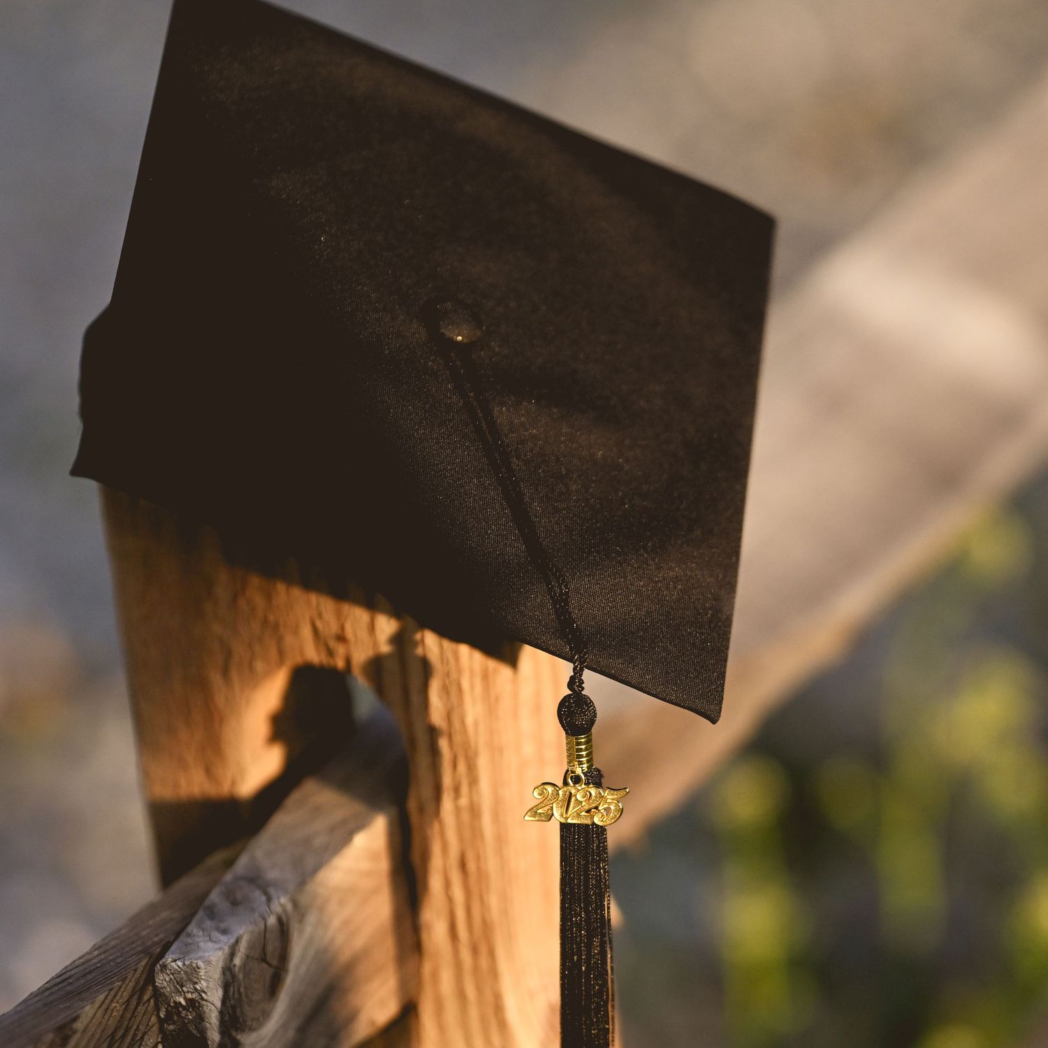 A black graduation cap with tassel sits atop a wooden post in golden sunlight.