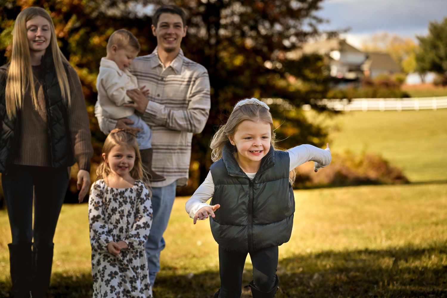 A family enjoys a candid moment together in a sunlit autumn field during golden hour.
