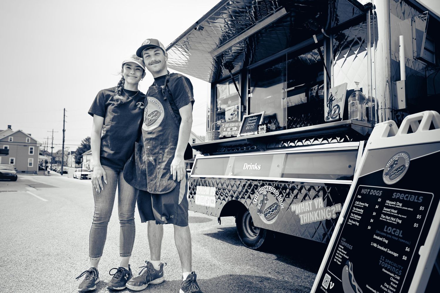 A black and white photo of two people standing in front of a food truck on a sunny day.