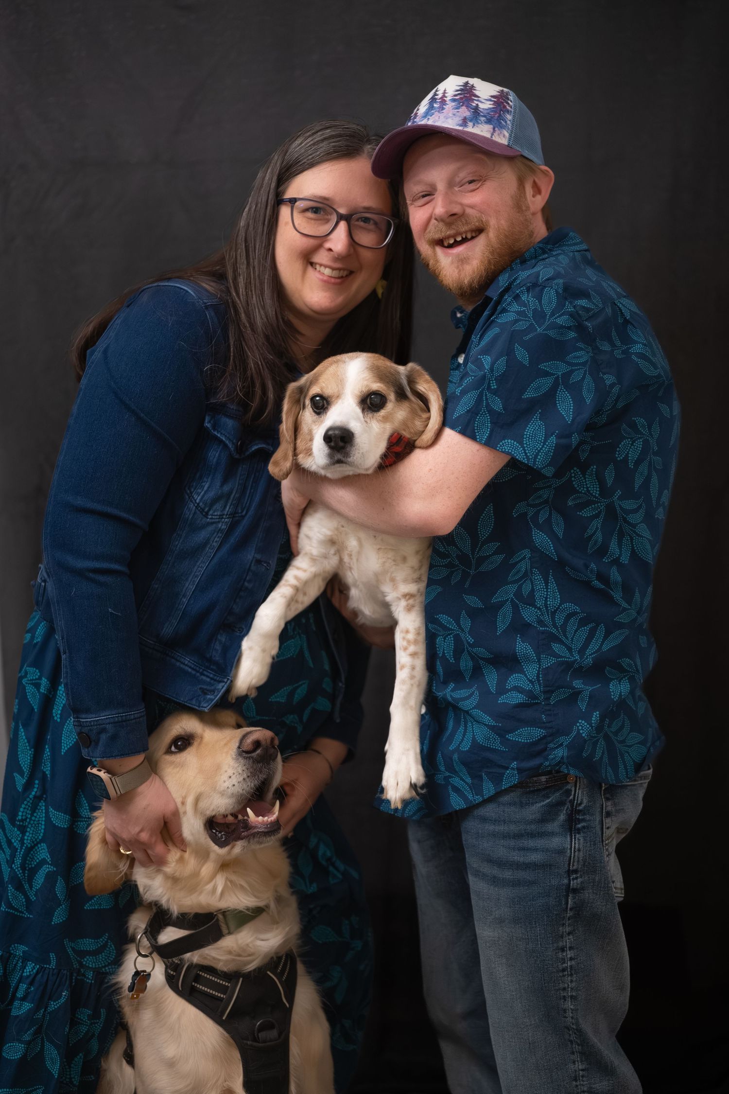 A couple poses with their beagle mix dog against a dark background in a series of affectionate portrait shots.