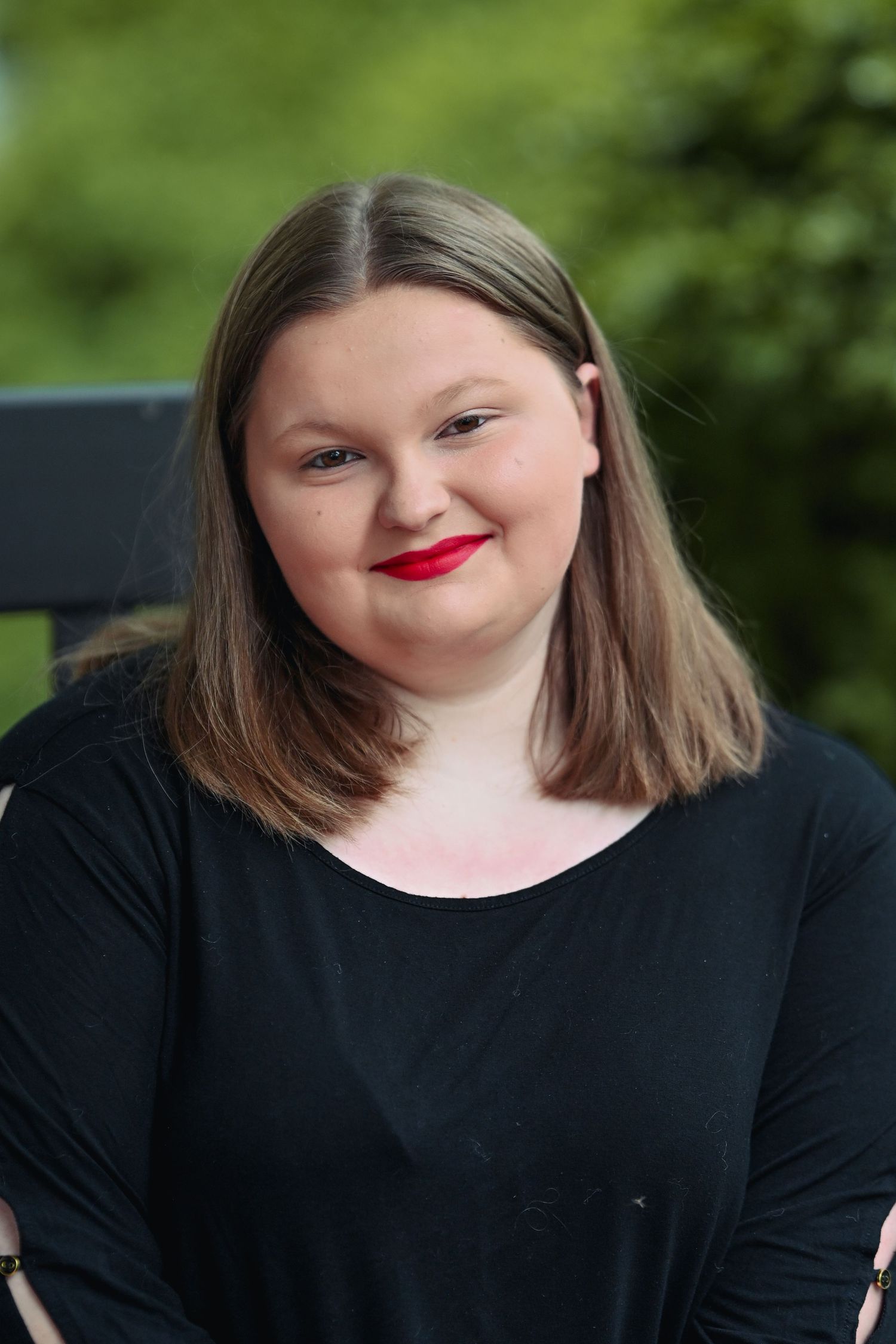 A figure in a black top wearing bright red lipstick is shown smiling through a series of progressive portrait shots outdoors.