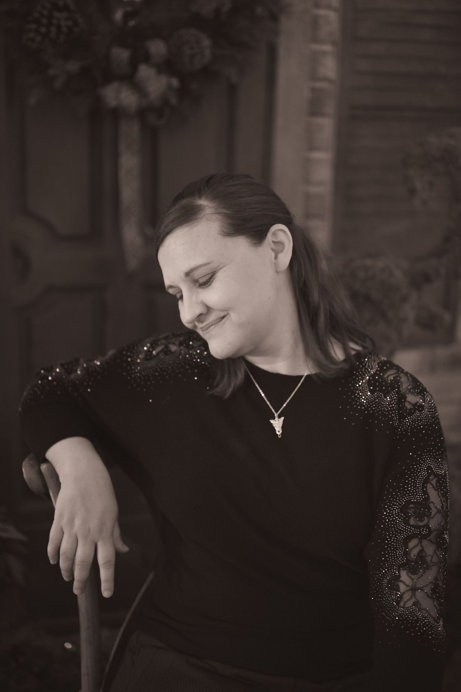 Black and white portrait of someone in a lace-sleeved sweater sitting with eyes closed and a gentle smile.
