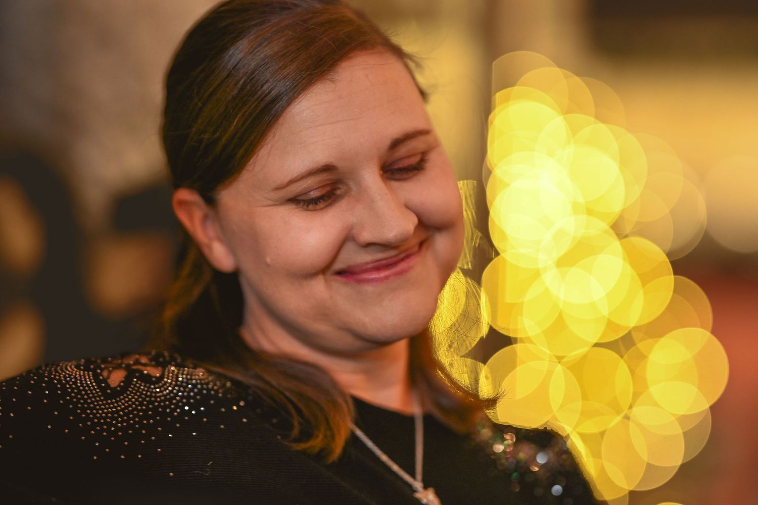 Someone smiling with glowing yellow bokeh lights in the background.