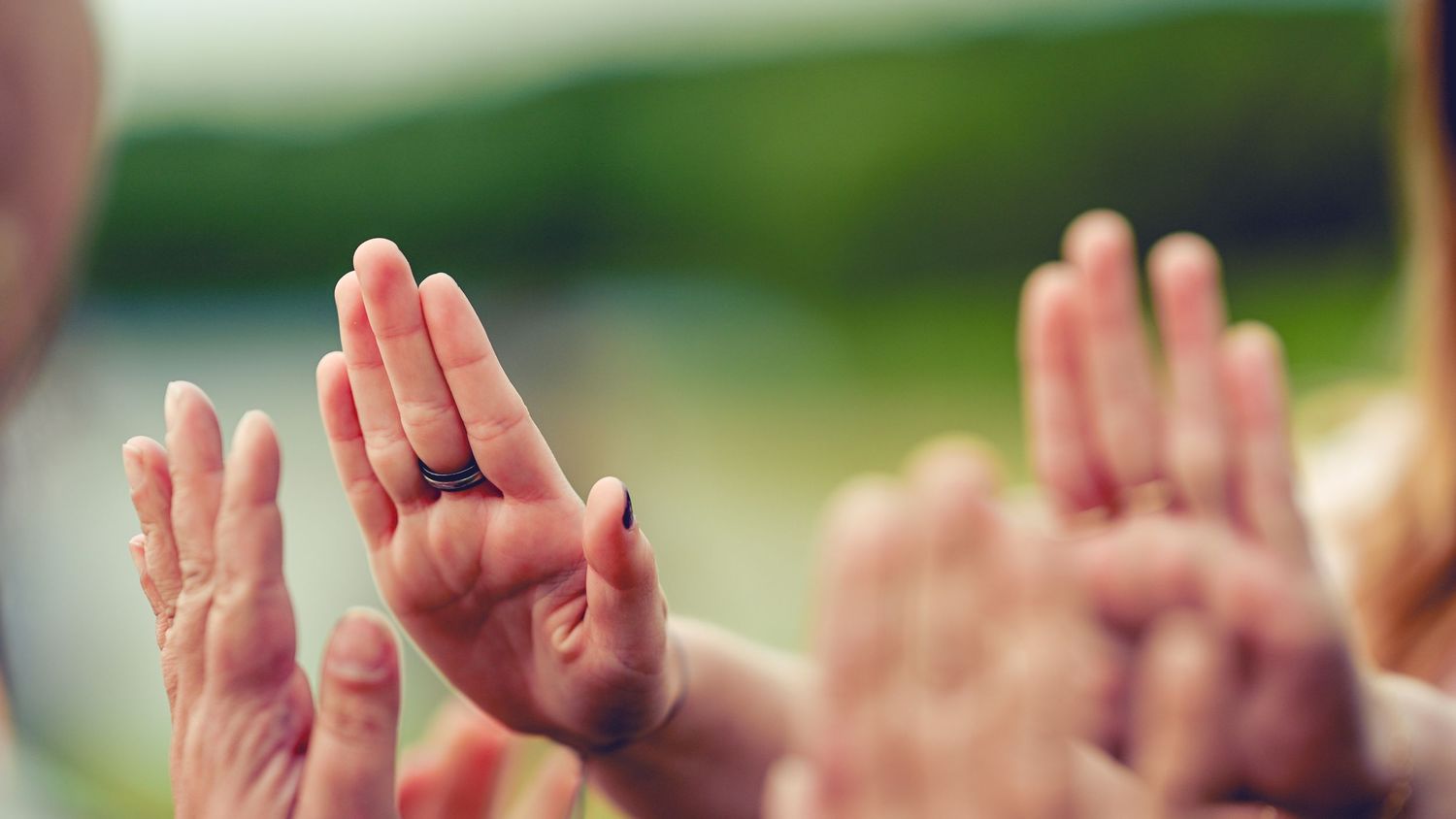 Raised hands with crossed fingers against a blurred outdoor background.