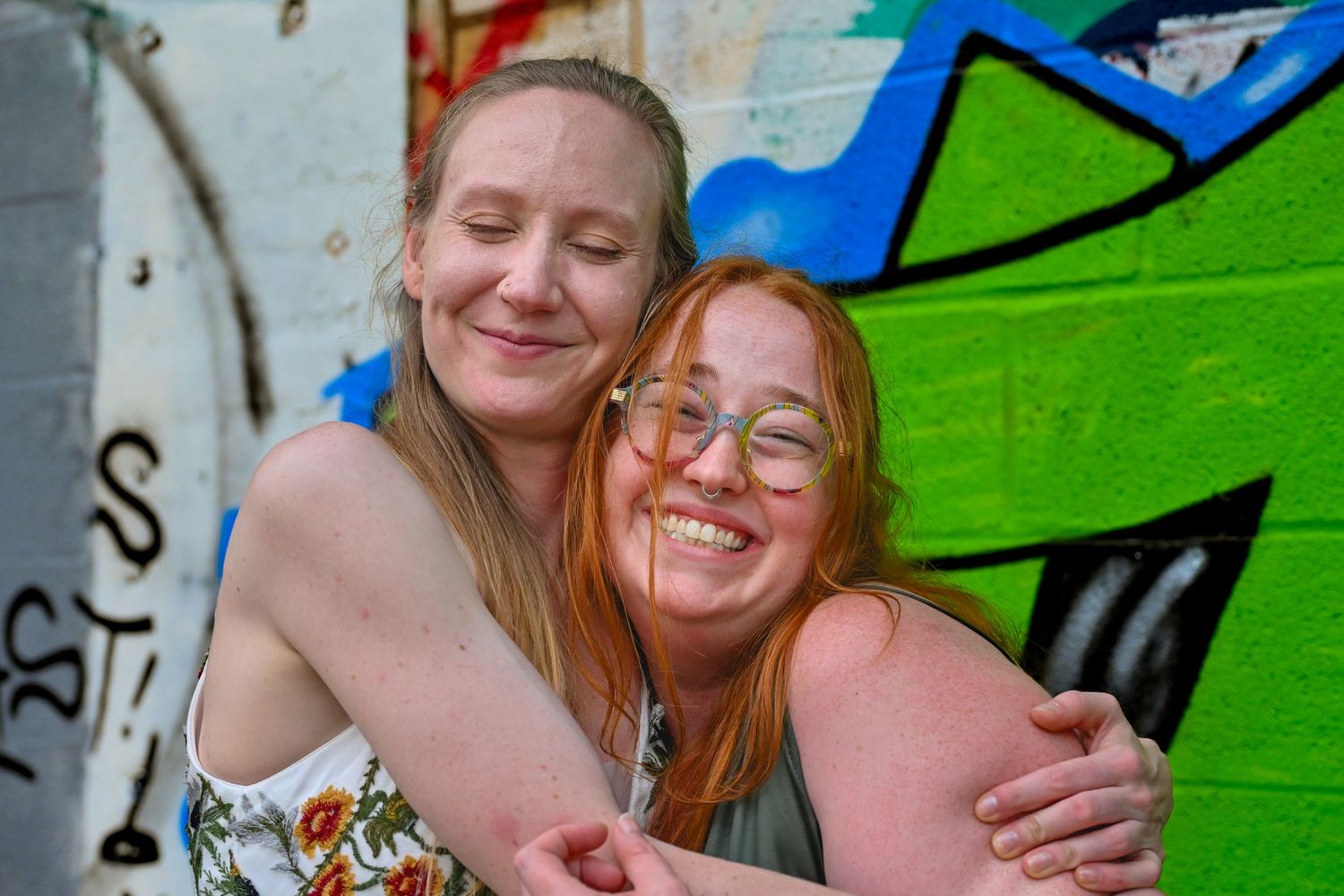Two friends share joyful moments in front of vibrant green graffiti art wall.