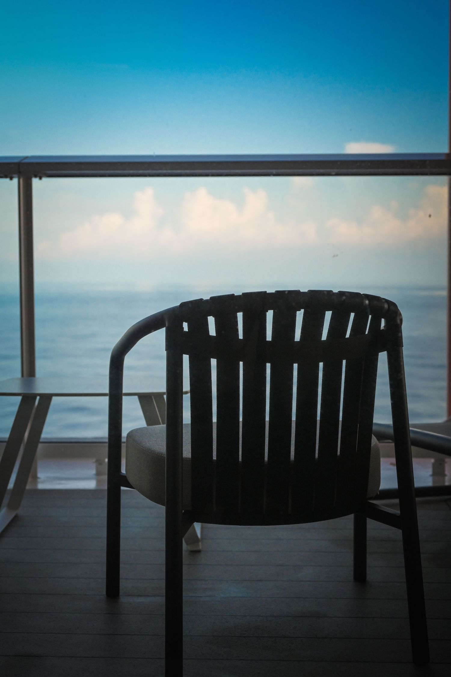 A wooden chair on a balcony overlooking a calm ocean under a blue sky with soft clouds at dusk.