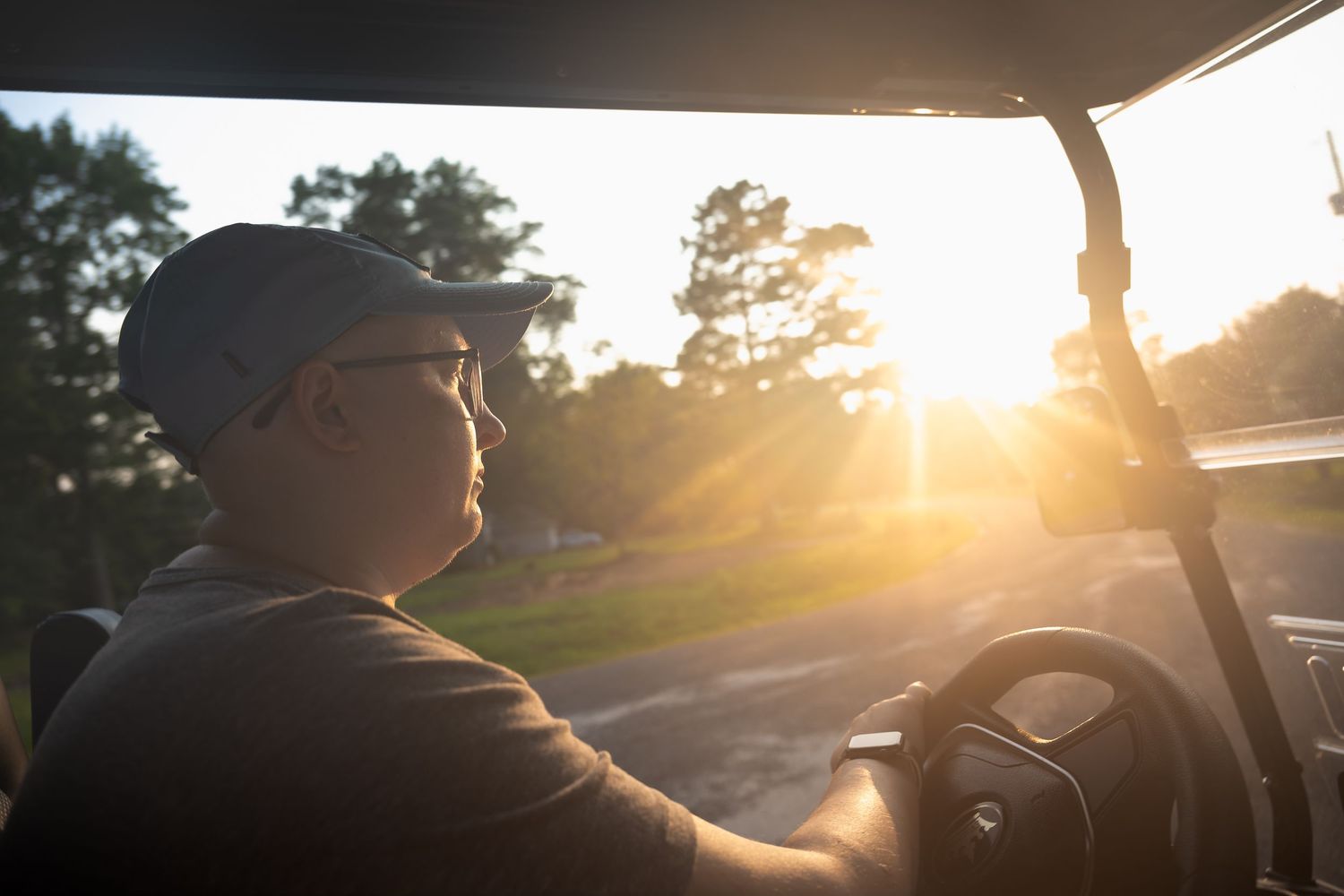 Man driving a golf cart at sunset with warm golden sunlight streaming through the trees.