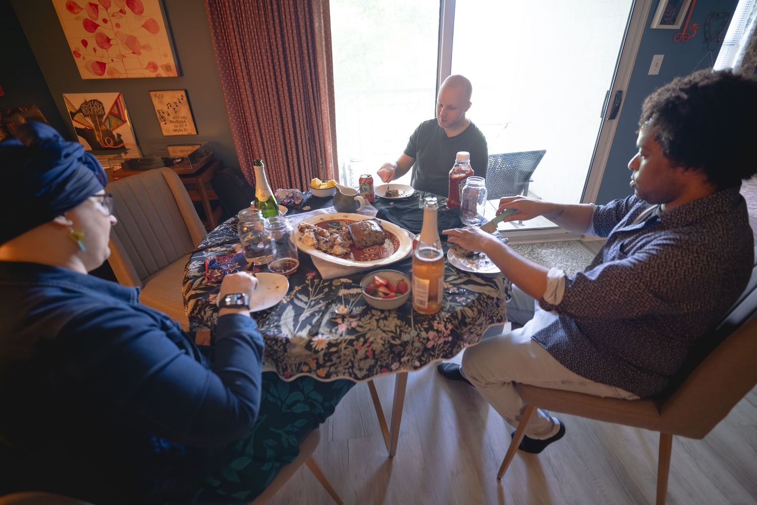 Three people sharing a meal around a dining table with food and drinks in a cozy indoor setting.